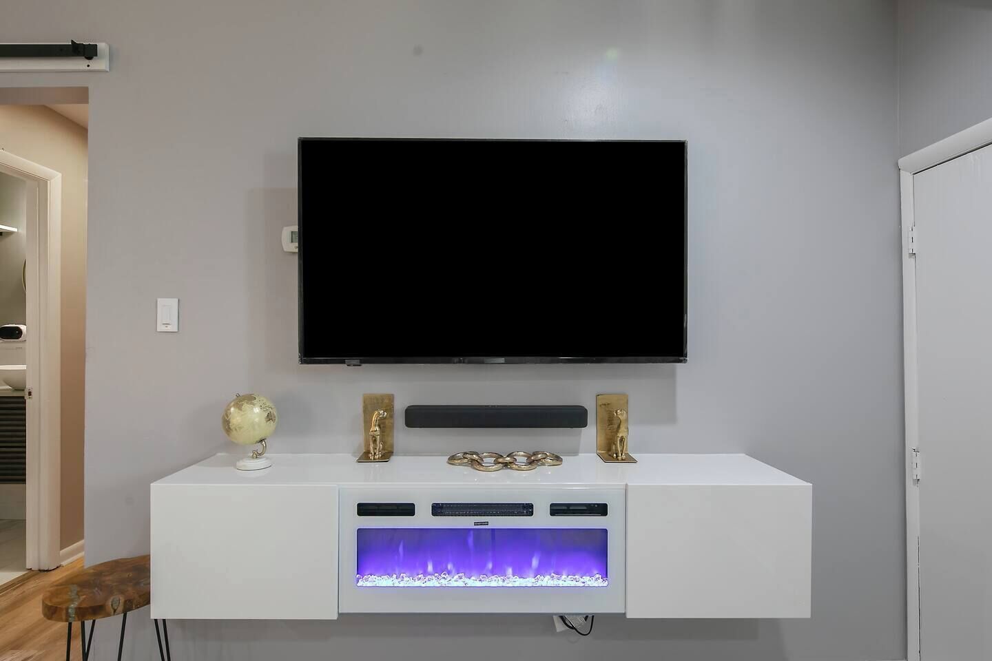 A modern living room with a mounted TV, a white entertainment unit with a built-in fireplace, and decorative items.