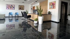 A modern reception area with a polished black floor, a reception desk, blue chairs, and framed artwork on the walls. - Hotel Blue Sky (Tarrafal)