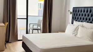 A modern hotel room with a large bed, wooden flooring, and a view of a building through the window. - Hotel Blue Sky (Tarrafal)