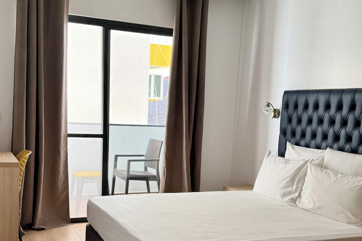 Habitación de hotel moderna con una cama grande, suelo de madera y vista a un edificio a través de la ventana.