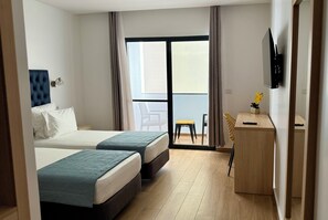 A hotel room with two beds, a desk, a chair, a TV, and a balcony with a view. - Hotel Blue Sky (Tarrafal)