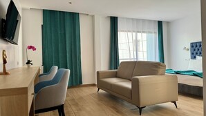 A modern hotel room with a wooden desk, two chairs, a beige sofa, and a bed with a blue headboard. - Hotel Blue Sky (Tarrafal)