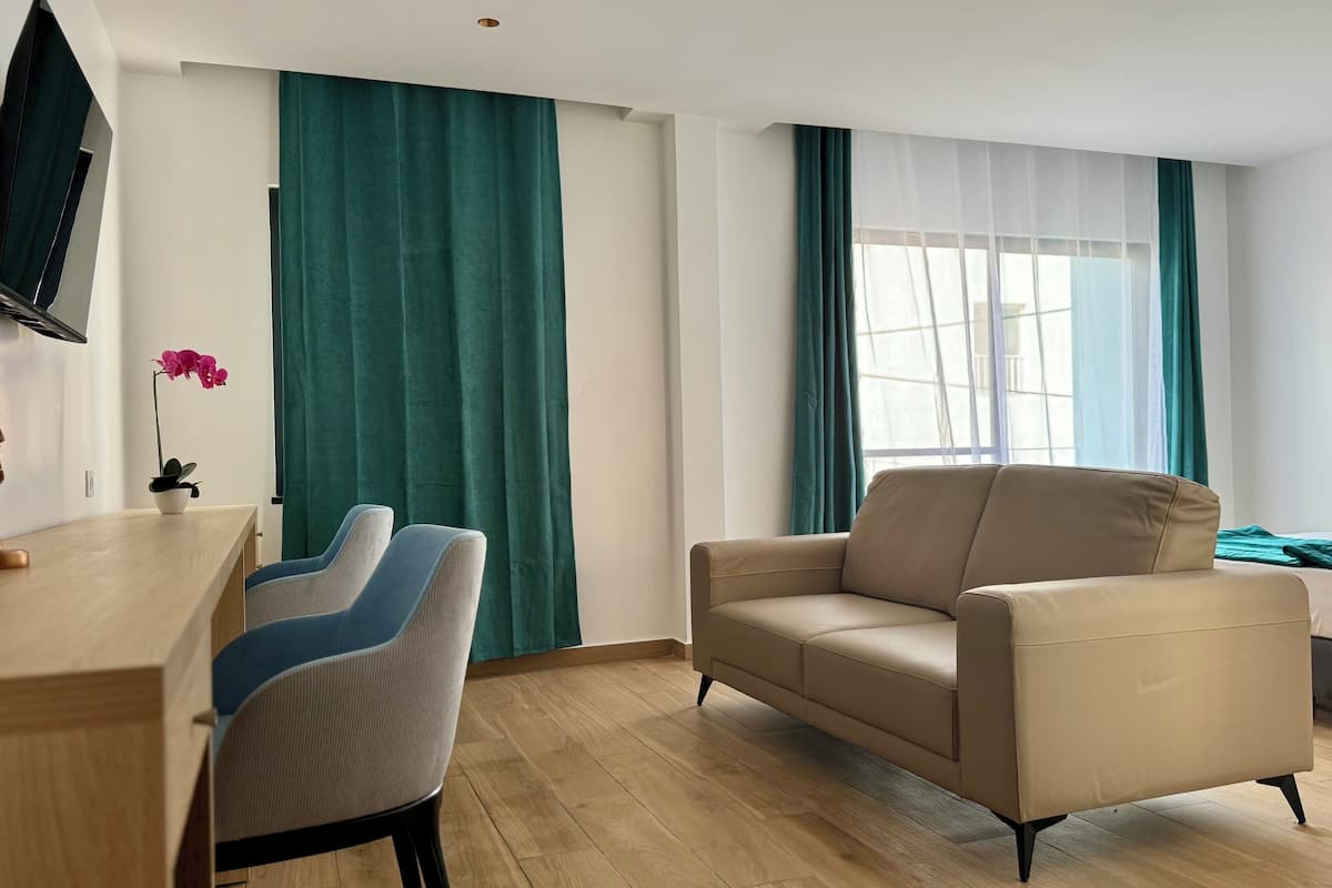 Una habitación de hotel moderna con un escritorio de madera, dos sillas, un sofá color crema y una cama con cabecera azul.