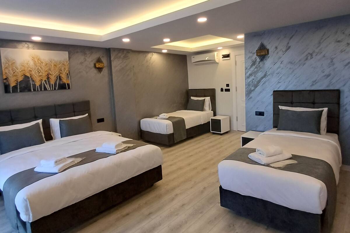 A modern hotel room with three beds, a marble wall, and recessed ceiling lighting.