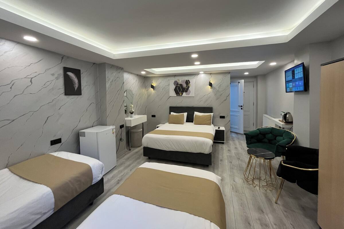 A modern hotel room with three beds, a desk, a chair, and a TV.