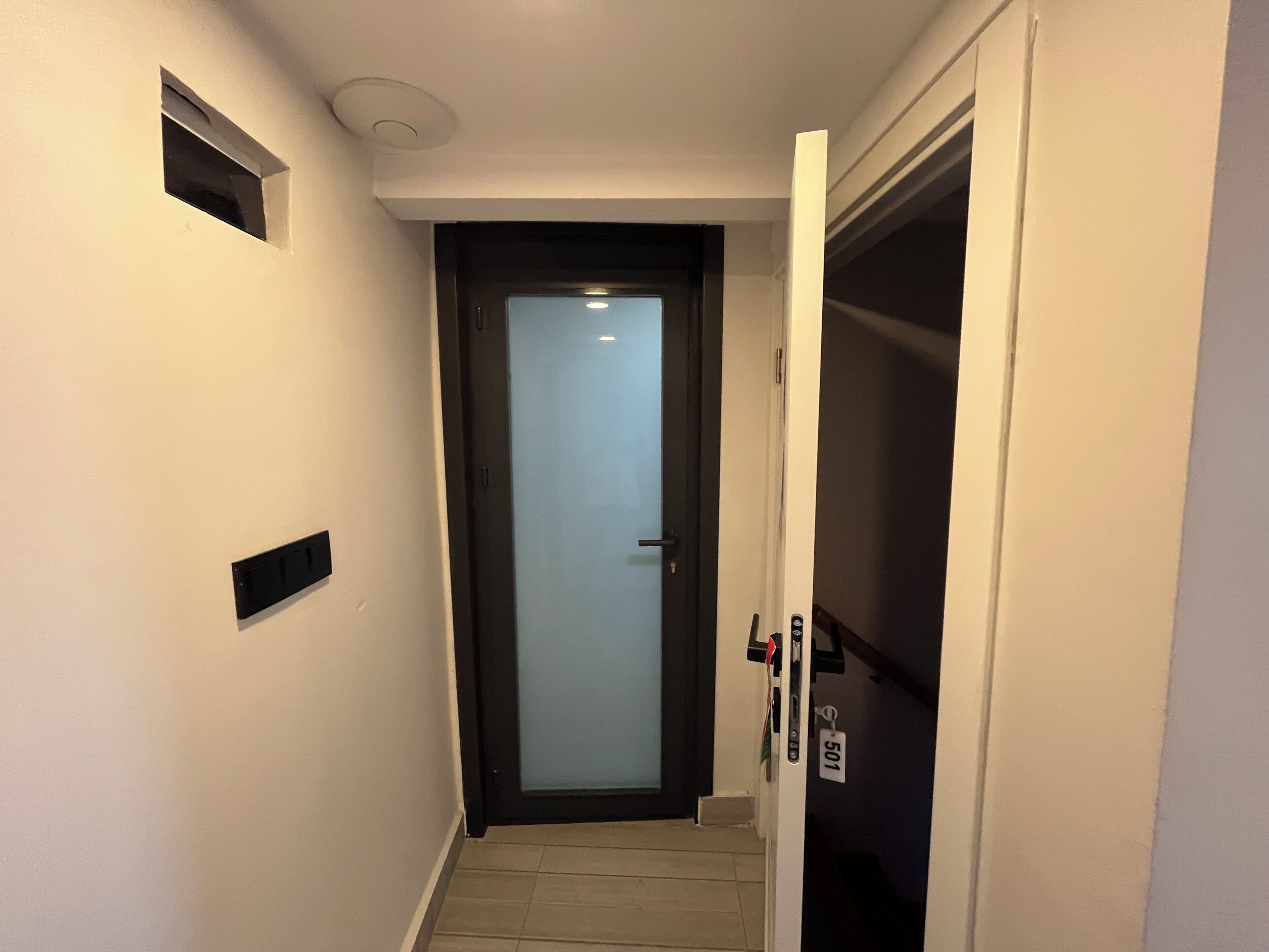 A narrow hallway with a door at the end, a small vent on the wall, and a keycard reader next to the door.