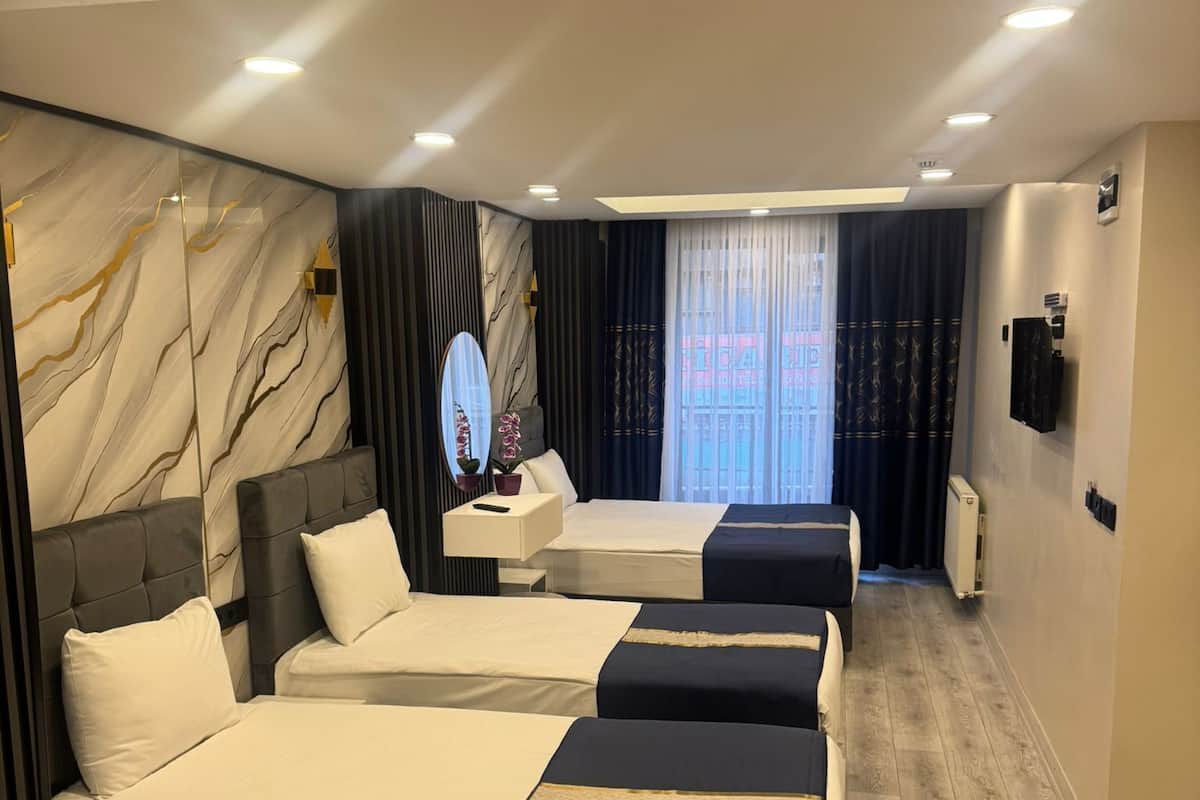 A hotel room with four beds, a marble wall, a large mirror, and a view of the city.