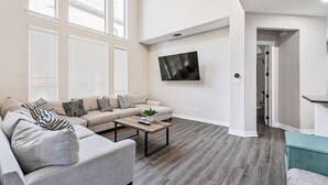 Ein modernes Wohnzimmer mit einer Couch, einem Couchtisch und einem an der Wand montierten Flachbildfernseher.