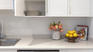Una cocina con armarios blancos, un lavamanos de acero inoxidable, un florero con flores y un bol con limones.