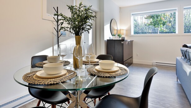 Un comedor moderno con una mesa de cristal, sillas negras y un florero con follaje.