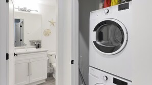 Un lavadero con dos lavadoras de carga frontal apiladas, un lavamanos blanco y una decoración de estrella de mar en la pared.