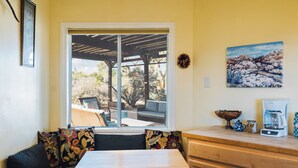 A cozy seating area with a table and bench, a window with a view of outdoor furniture, and a kitchen counter with a coffee maker. - 5 Miles from Park entrance Charming 2-bedroom house in enchanting Joshua Tree (Joshua Tree)