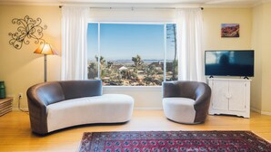 A living room with a large window, two sofas, a TV, and a decorative wall piece. - 5 Miles from Park entrance Charming 2-bedroom house in enchanting Joshua Tree (Joshua Tree)