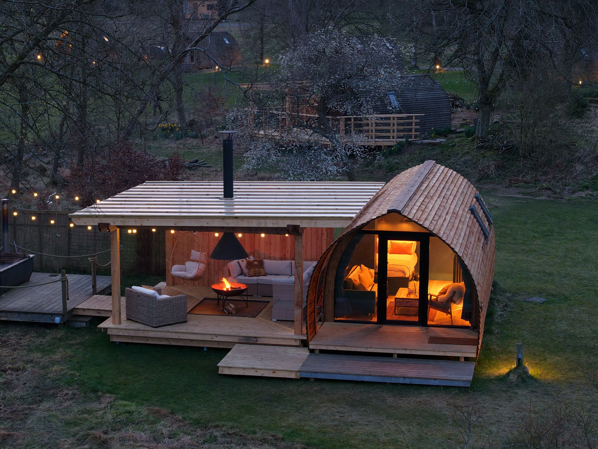A cozy, semi-open wooden structure with a fireplace, seating area, and string lights.