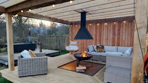A covered outdoor seating area with wicker furniture, a hanging light fixture, and a fire pit. - Luxury Rural Cabin with Wood Fired Hot Tub (Leven)
