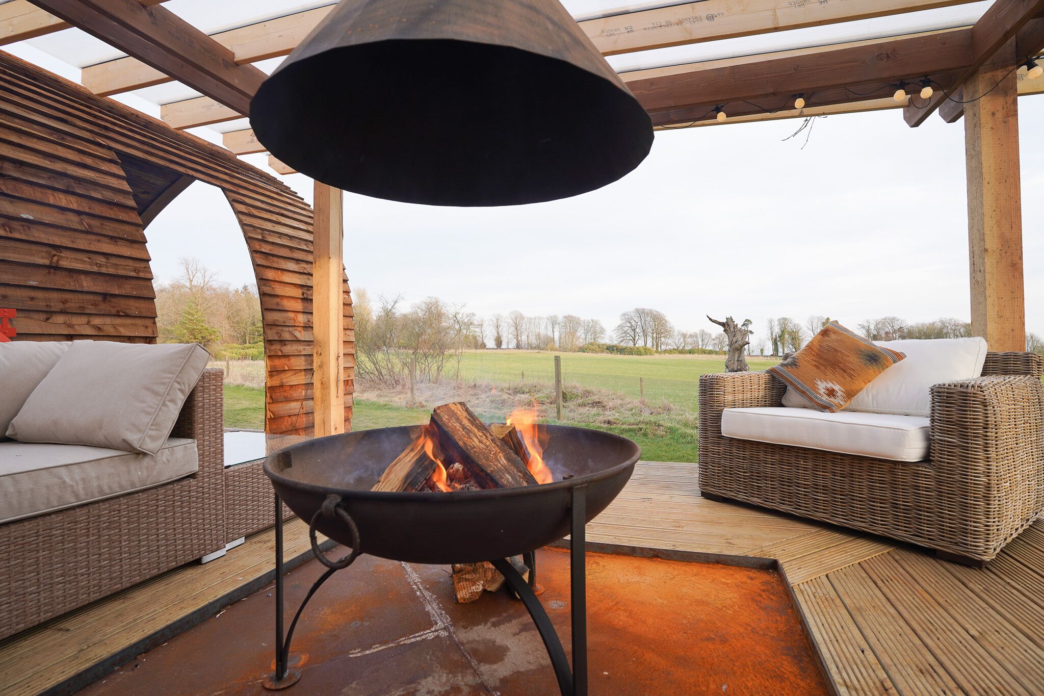 Een terras met een vuurkorf, rieten meubels en uitzicht op het omliggende landschap.