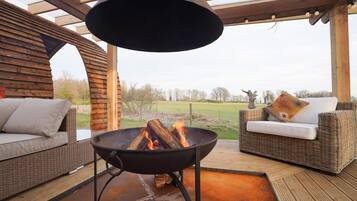 Een terras met een vuurkorf, rieten meubels en uitzicht op het omliggende landschap.