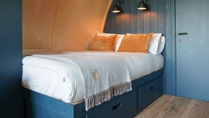 Ein Bett mit weißer Matratze, orangefarbenen Kissen, einem blauen Kopfteil und einem kleinen Nachttisch mit Schublade.