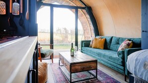 Ein gemütliches Interieur mit gewölbter Decke, einem grünen Sofa, einem Holztisch und Blick durch ein großes Fenster.