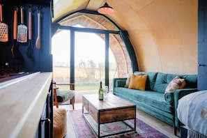 A cozy interior with a curved ceiling, a green sofa, a wooden coffee table, and a view through a large window.