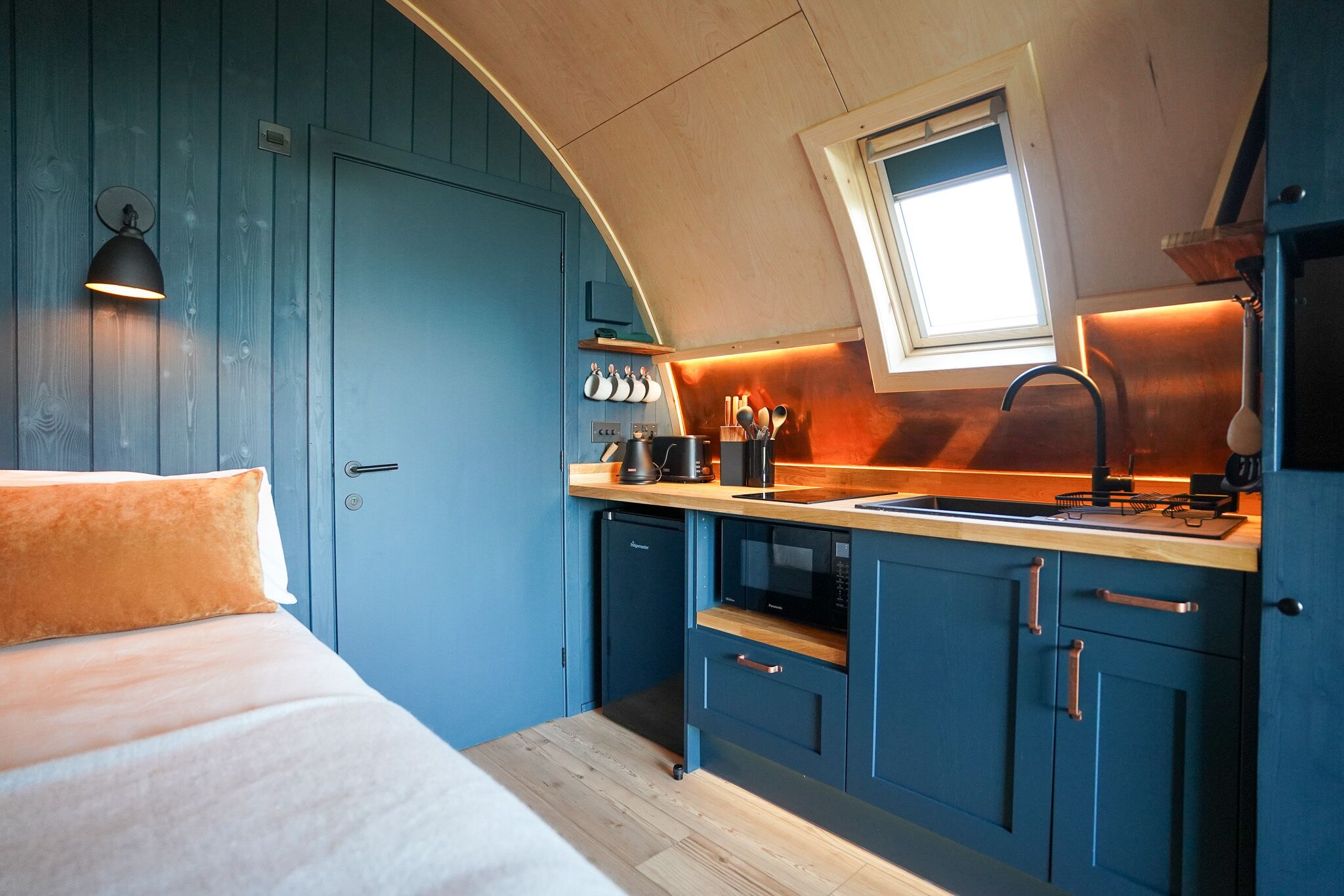 A compact kitchen with blue cabinets, a wooden countertop, and a window above the sink.