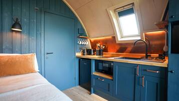A compact kitchen with blue cabinets, a wooden countertop, and a window above the sink.