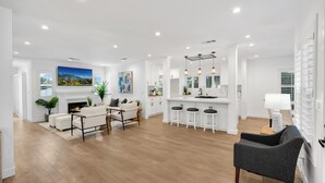 Un vaste espace de vie comprenant un coin salon avec cheminée, un coin repas et une cuisine avec des tabourets de bar.