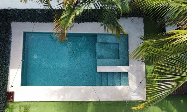 Ein rechteckiger Swimmingpool mit Stufen, umgeben von einer weißen Mauer und einer grünen Umrandung.