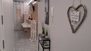 Un pasillo con baldosas de diseño, una puerta blanca, una pequeña mesa con plantas y una decoración en forma de corazón con un símbolo de WiFi.