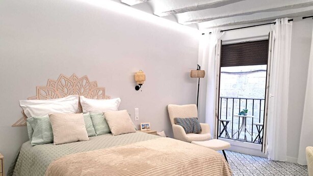 Un dormitorio con una cama grande, una silla, un balcón con una mesa y un suelo estampado.