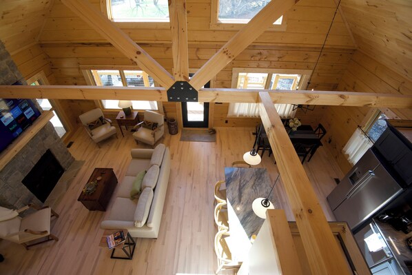 A spacious loft with a high ceiling, wooden beams, a living area with a sofa and chairs, a dining area, and a kitchen.