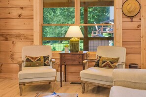 A cozy room with two armchairs, a small table with a lamp, and a window with a view of greenery outside.