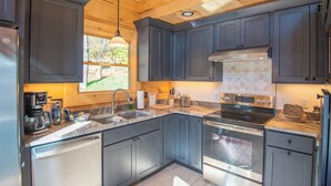 Cocina moderna con armarios oscuros, estufa de acero inoxidable y un amplio ventanal que proporciona luz natural.