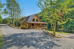 A wooden cabin with a sloped roof, a covered porch, and a gravel driveway.