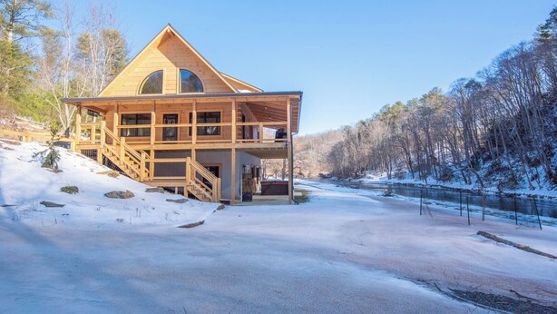 Een ruime houten chalet met een balkon, gelegen op een sneeuwbedekte helling met een rivier op de achtergrond.