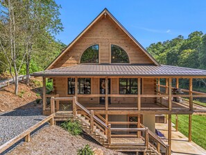 A wooden cabin with a large front porch, a covered deck, and a staircase leading to the main entrance.