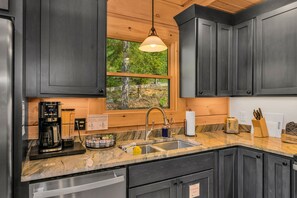 Une cuisine moderne avec des meubles de couleur sombre, un plan de travail en marbre, un lave-vaisselle encastré et une fenêtre donnant sur un paysage verdoyant.