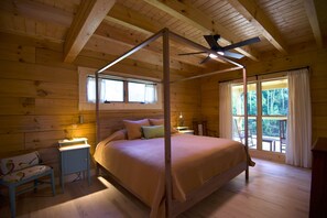 A wooden cabin bedroom with a four-poster bed, a desk with a chair, and a window with curtains.