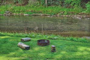 A natural outdoor setting with a pond, rocks, and a metal container on the grass.