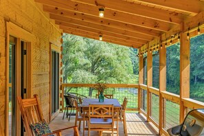 A wooden deck with a table and chairs, a grill, and a view of trees.