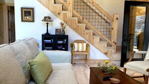 Amplia sala de estar con escalera de madera, un sofá, una mesa de centro y una estantería.