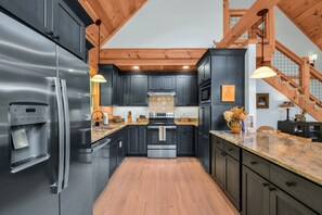 A modern kitchen with dark cabinetry, stainless steel appliances, and a wooden ceiling.
