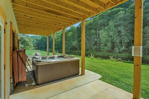 Un espace extérieur abrité avec un jacuzzi, doté d’une terrasse en bois, entouré d’un paysage verdoyant luxuriant et bordé par une rivière.