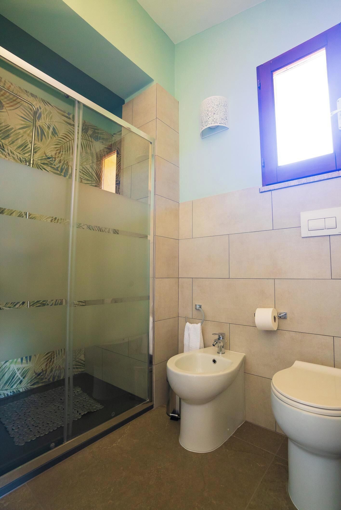 A bathroom with a glass shower enclosure, a bidet, and a toilet.