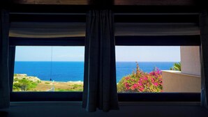 Habitación con un ventanal grande que ofrece vistas a un paisaje costero, con una vista despejada del mar y vegetación distante.