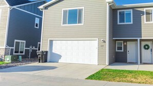 A two-story residential building with a white garage door, a small front porch, and a mailbox.
