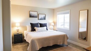 A bedroom with a bed, two bedside tables, a window, and two wall-mounted pictures.