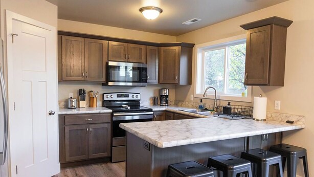 A modern kitchen with dark wooden cabinets, stainless steel appliances, a marble countertop, and a window providing natural light.