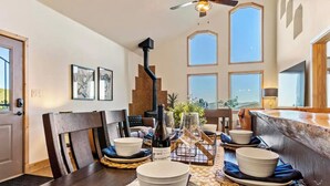 A dining area with a high ceiling, large windows, and a view of the outdoors.