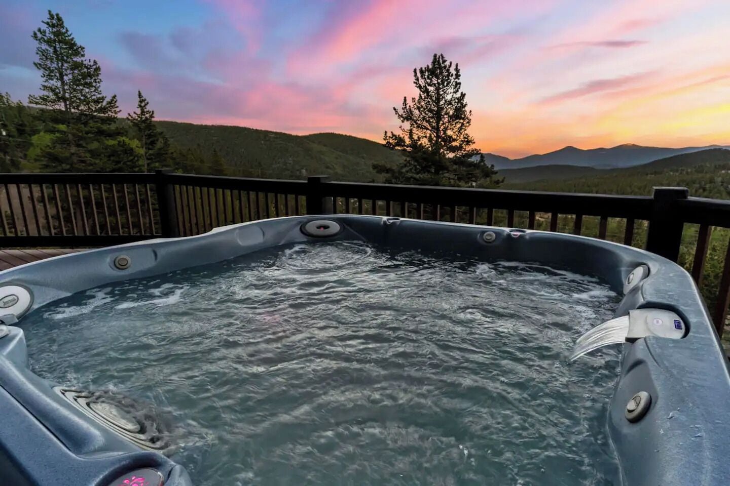 Un bain à remous avec une terrasse en bois et une vue imprenable sur les montagnes au coucher du soleil.